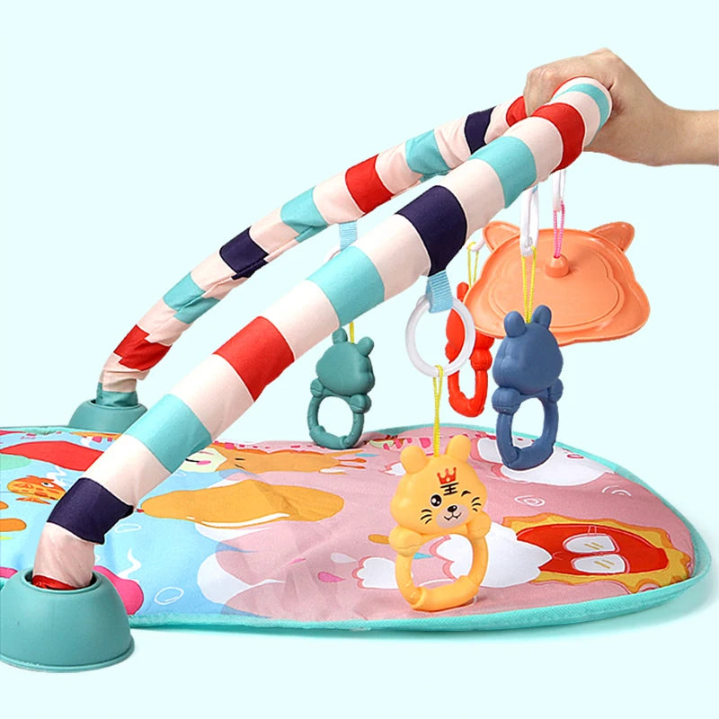 Colorful baby play mat with a striped arch and hanging toys, including animal rings in blue and orange. A hand holds the arch, showing its flexibility.