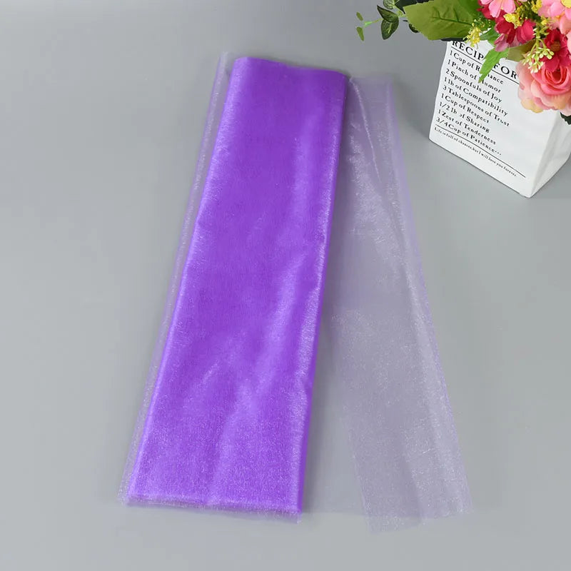 Purple and translucent mesh fabric pieces on a gray surface. To the side, a bag with pink roses and green leaves adds a decorative touch.