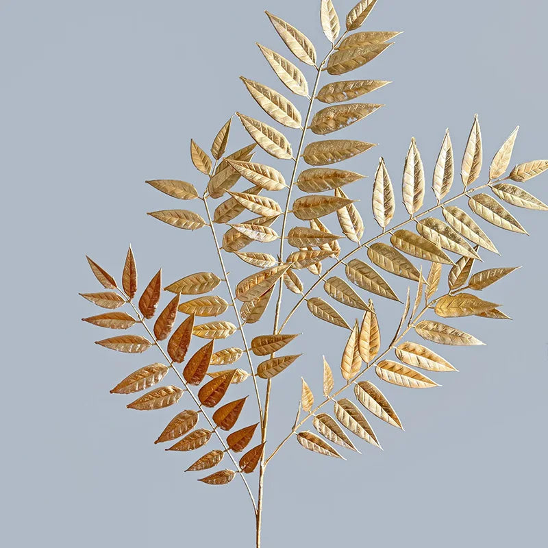 Elegant golden-brown leaves with a detailed veined pattern, arranged in a spray against a plain gray background, creating a striking and minimalist botanical composition.