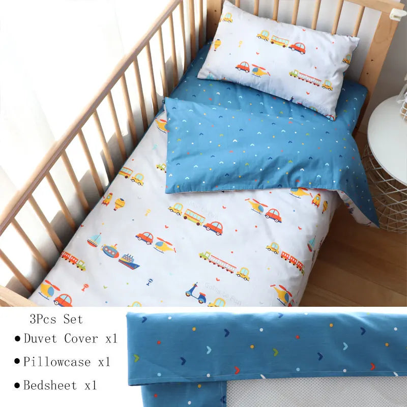 Children's bedding set with a white duvet cover and pillowcase featuring colorful vehicles and a blue sheet with small patterns, displayed in a wooden crib.
