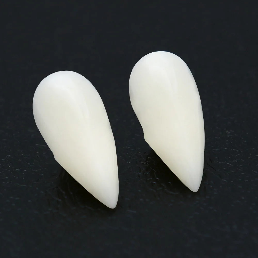 Two realistic, white, pointed fake vampire fangs displayed on a dark surface, mimicking natural teeth and designed for costume use.