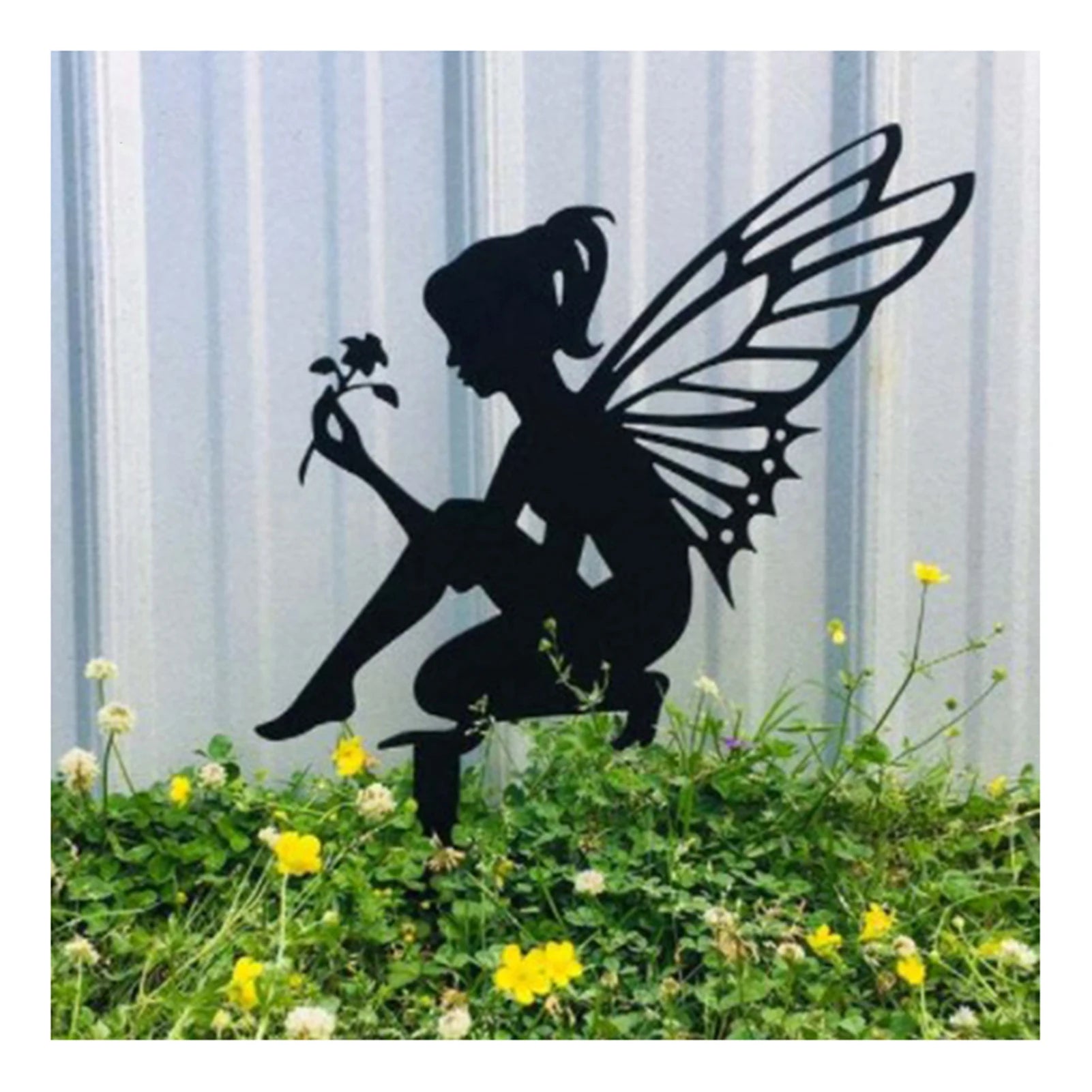 Silhouette of a fairy crouching, holding a flower, with intricate wings. The figure is set against a corrugated metal background and surrounded by grass and yellow flowers.