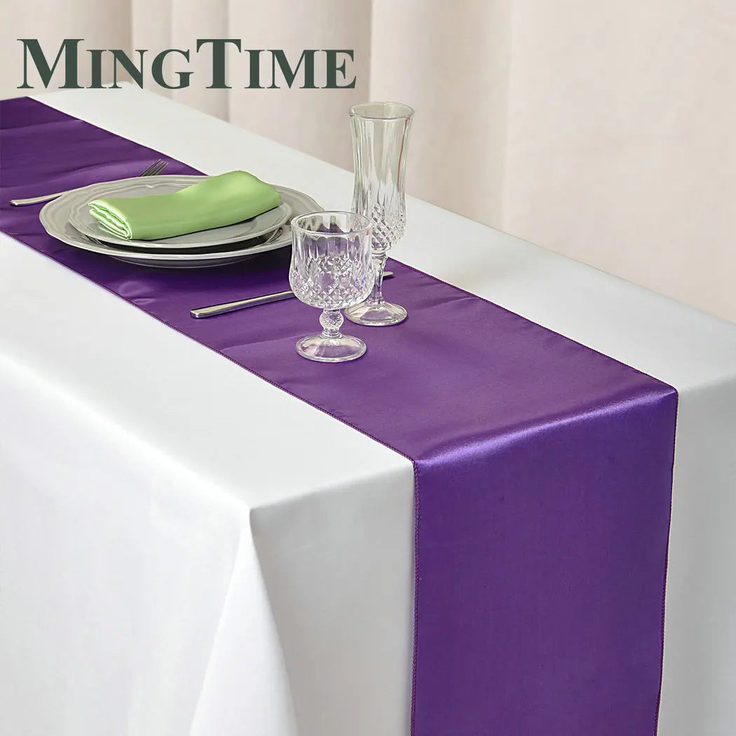 Elegant table setting with a white tablecloth and purple satin runner. Includes a plate with a light green napkin, silverware, and crystal glasses. "MingTime" text is displayed above.