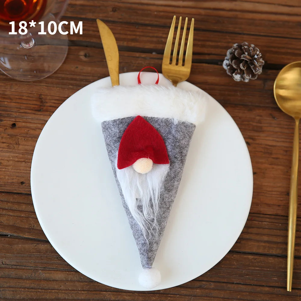 A festive gnome-themed cutlery holder on a white plate, featuring gold utensils. The gnome has a red hat, white beard, and cone shape. Wooden table and pinecone nearby.
