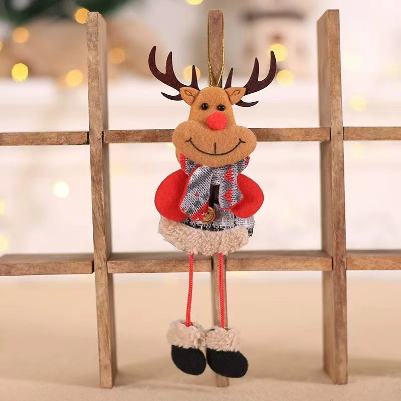 Plush reindeer ornament with antlers, red nose, and a warm scarf. It has red mittens, furry boots, and is seated on a wooden shelf backdrop with festive lighting.