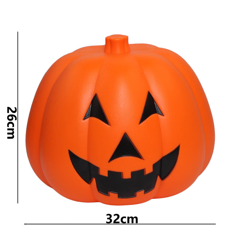 Orange pumpkin decoration with a carved smiling face, featuring triangular eyes and a jagged mouth. Its dimensions are 26cm in height and 32cm in width.