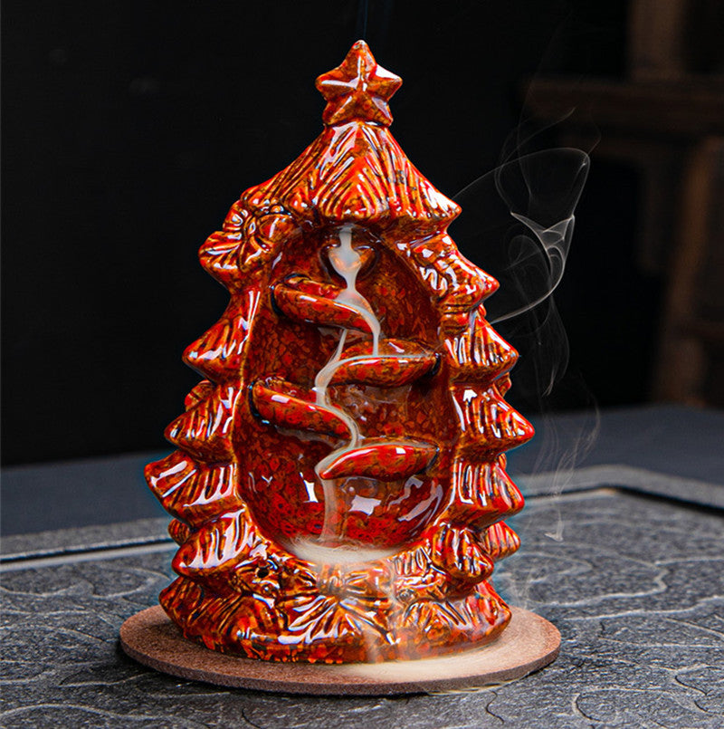 Ceramic incense holder shaped like a Christmas tree with cascading smoke, intricately designed with a glossy red finish and placed on a circular base.