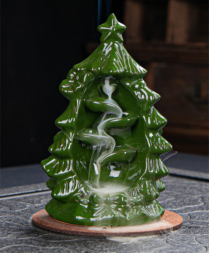 Green ceramic incense holder shaped like a Christmas tree emits white smoke along spiraling channels, placed on a textured surface.