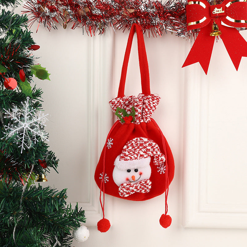 Red Christmas gift bag with snowman design, hanging on a white wall. Decorated with a red and white pattern, holly leaves, surrounded by festive garland and a Christmas tree.