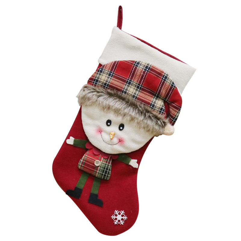 A festive Christmas stocking featuring a cheerful snowman in a plaid outfit with a fuzzy hat. The red sock includes green arms and pants, black shoes, and a white snowflake detail.