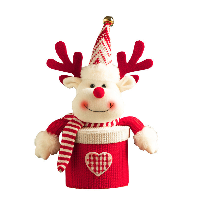 A plush reindeer ornament with red antlers and a striped scarf and hat, featuring a smiley face and white fur. It sits on a red container with a gingham heart pattern.