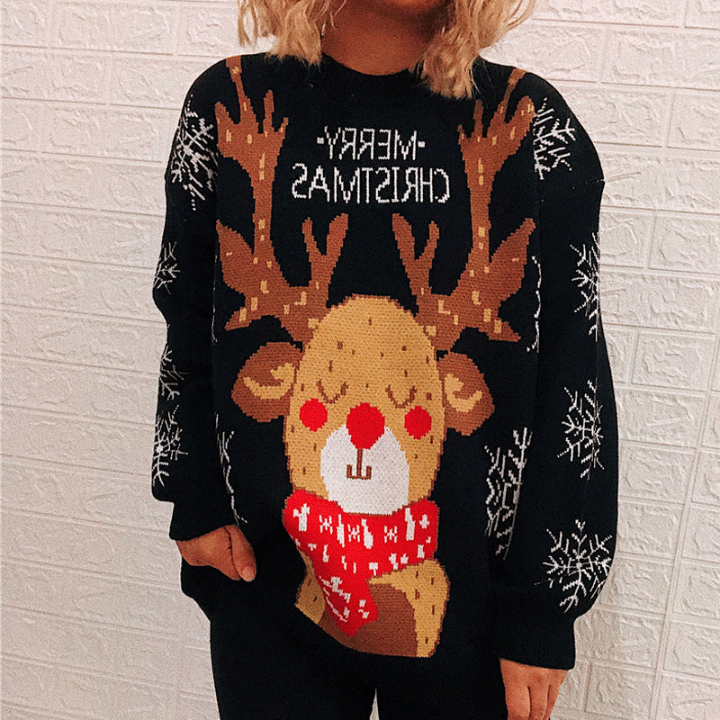 Person wearing a festive sweater featuring a cheerful reindeer with a red nose, red scarf, and "Merry Christmas" text in reverse. Snowflake patterns on sleeves, white brick background.