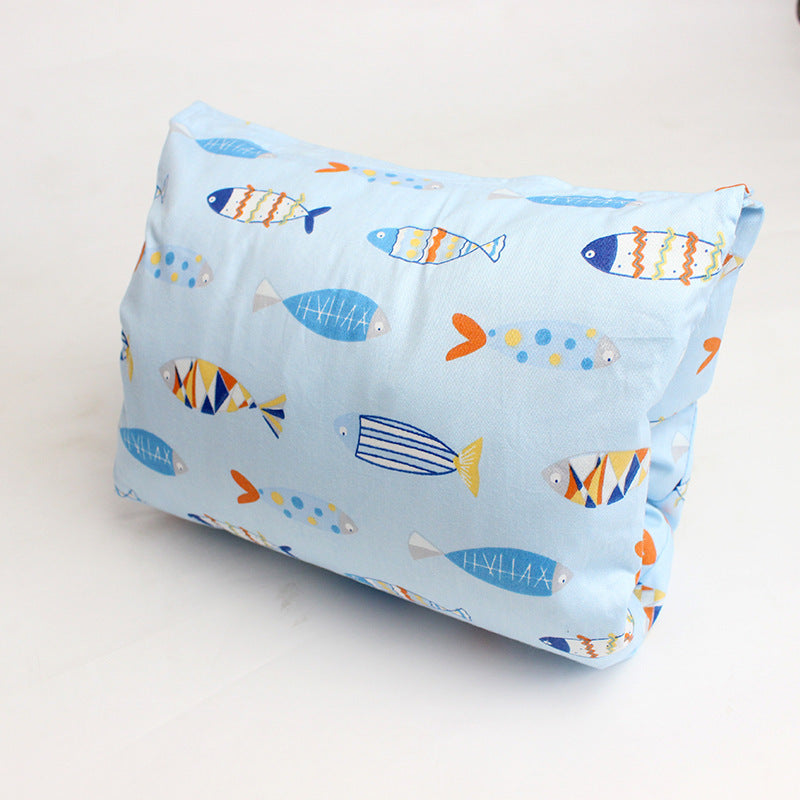 Light blue pillow with colorful, stylized fish patterns in orange, blue, and yellow on a plain white surface. The fish have various striped and dotted designs.