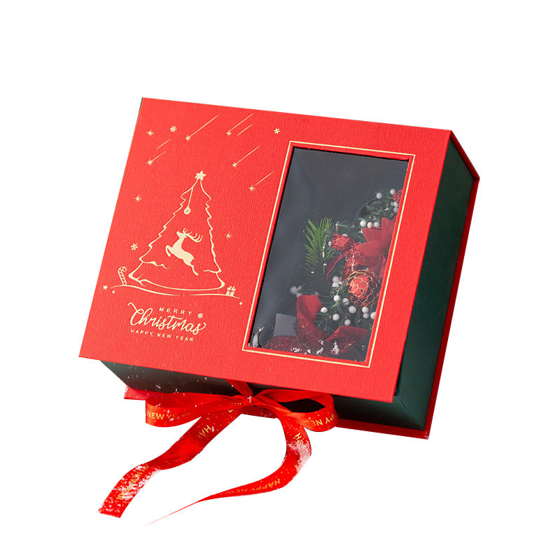Red Christmas gift box with a window showing festive decorations inside. The lid features a golden tree design with a reindeer and "Merry Christmas, Happy New Year" text.