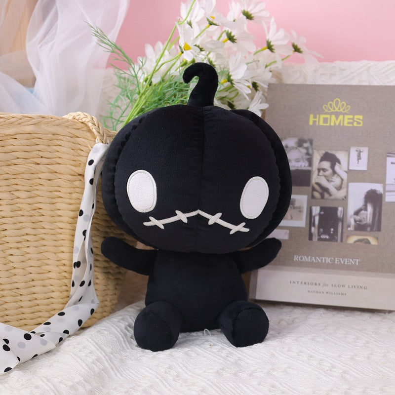A black, round plush toy with large white eyes and a stitched mouth sits on a textured surface. It leans against a wicker basket with a polka-dot ribbon and is surrounded by flowers.