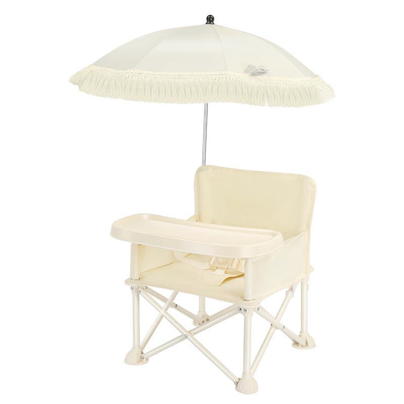 Portable baby high chair with a tray, beige fabric seat, and a collapsible frame. Includes a large, detachable cream umbrella for shade, adorned with fringe lining.
