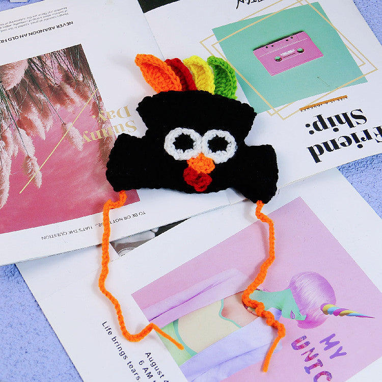 Crocheted black bat with colorful wings and googly eyes placed on scattered magazine pages featuring a pastel palette and various artistic designs.