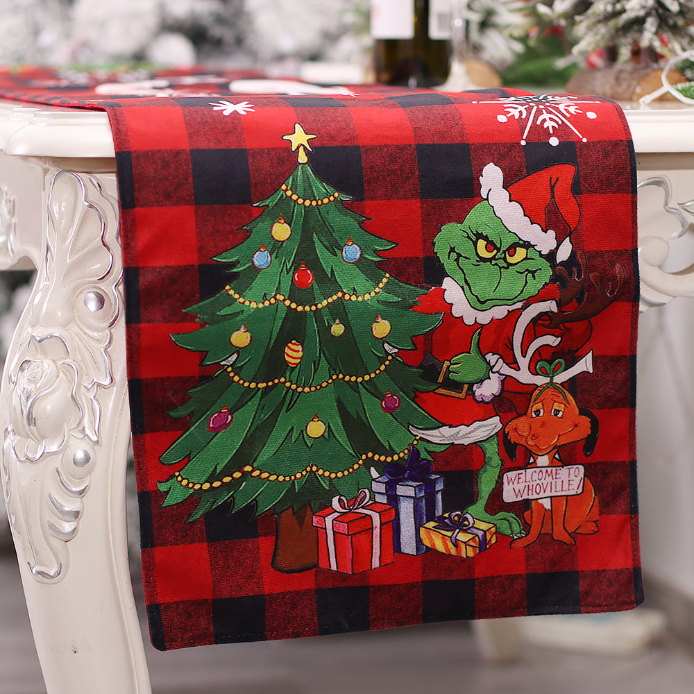 Festive table runner on a white table, featuring a Christmas tree with ornaments, gifts, and a character in a Santa outfit alongside a dog wearing reindeer antlers.