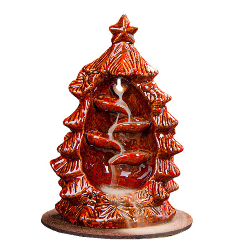 Ceramic incense holder shaped like a red Christmas tree, with smoke cascading down a tiered path inside, set on a round base.