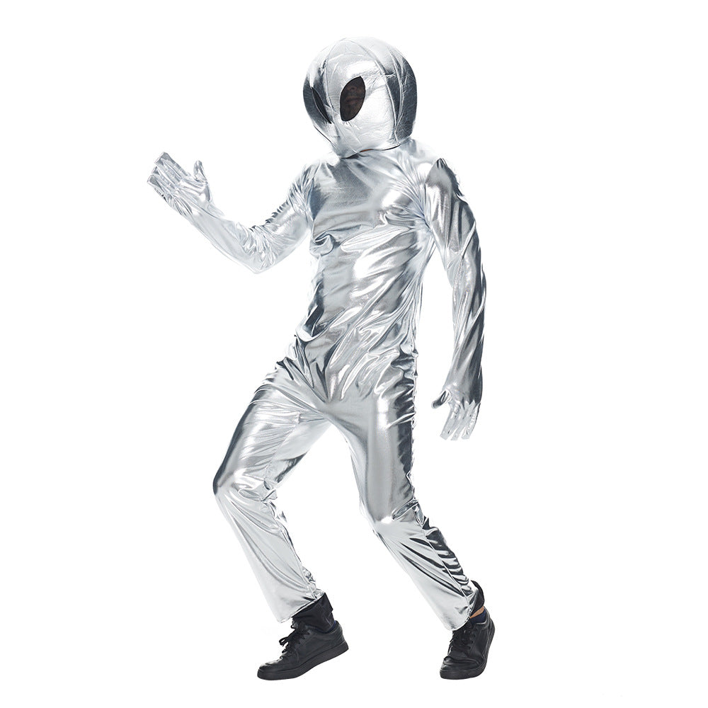 A person in a shiny silver alien costume with a smooth, metallic texture poses against a plain white background. The costume features a helmet with large, dark eye areas, and the individual is wearing black shoes, striking a dynamic, forward-moving pose.