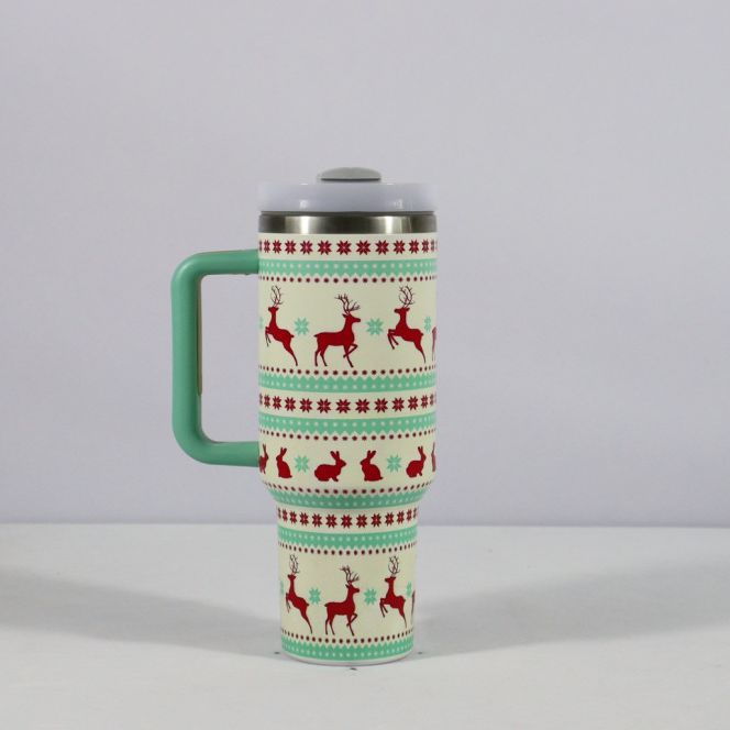 Festive travel mug with green handle, featuring red reindeer and bunny patterns, snowflakes, and decorative designs against a cream background.