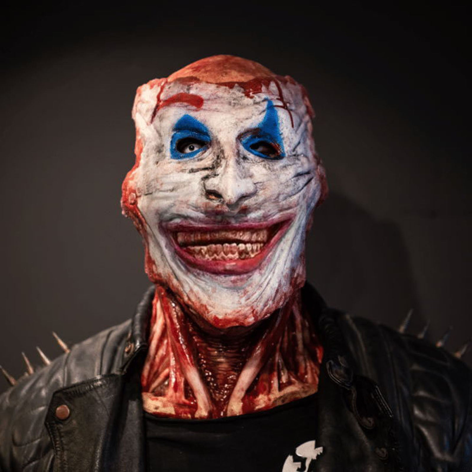 Creepy clown with a sinister grin, wearing a leather jacket and spike details. Blood and gruesome marks cover the face and neck, creating a horror-themed appearance.