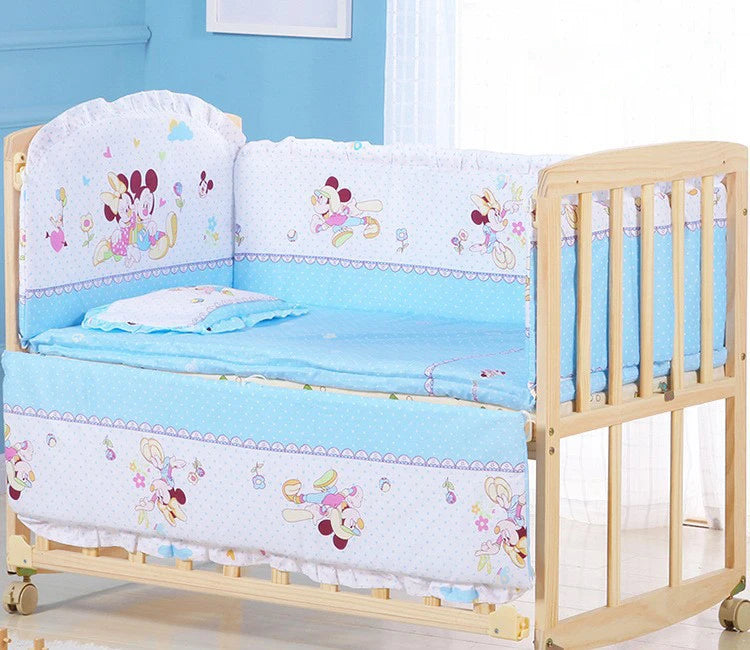 Wooden baby crib with blue bedding featuring cartoon characters, set in a light blue room.