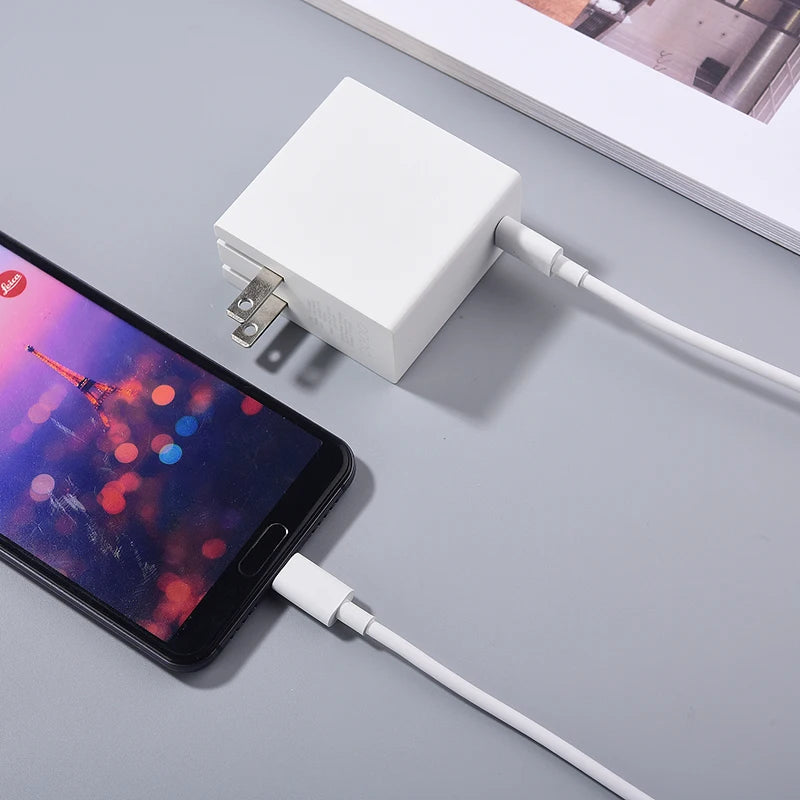 Smartphone charging with a white wall adapter on a gray surface, displaying a blurred cityscape with the Eiffel Tower on its screen.