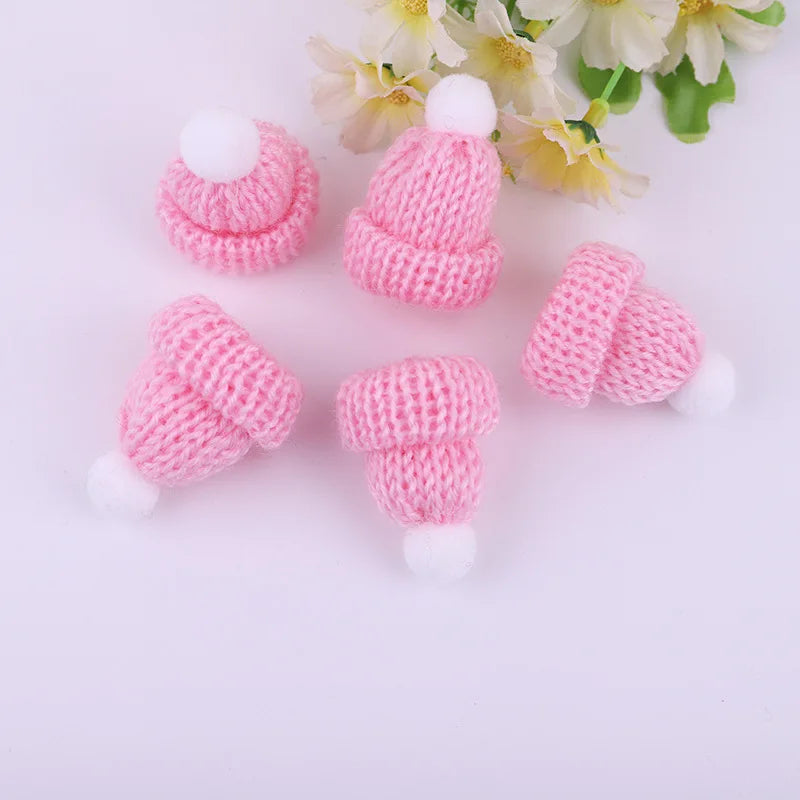 Five small pink knitted hats with white pom-poms, arranged on a surface near yellow and white flowers.