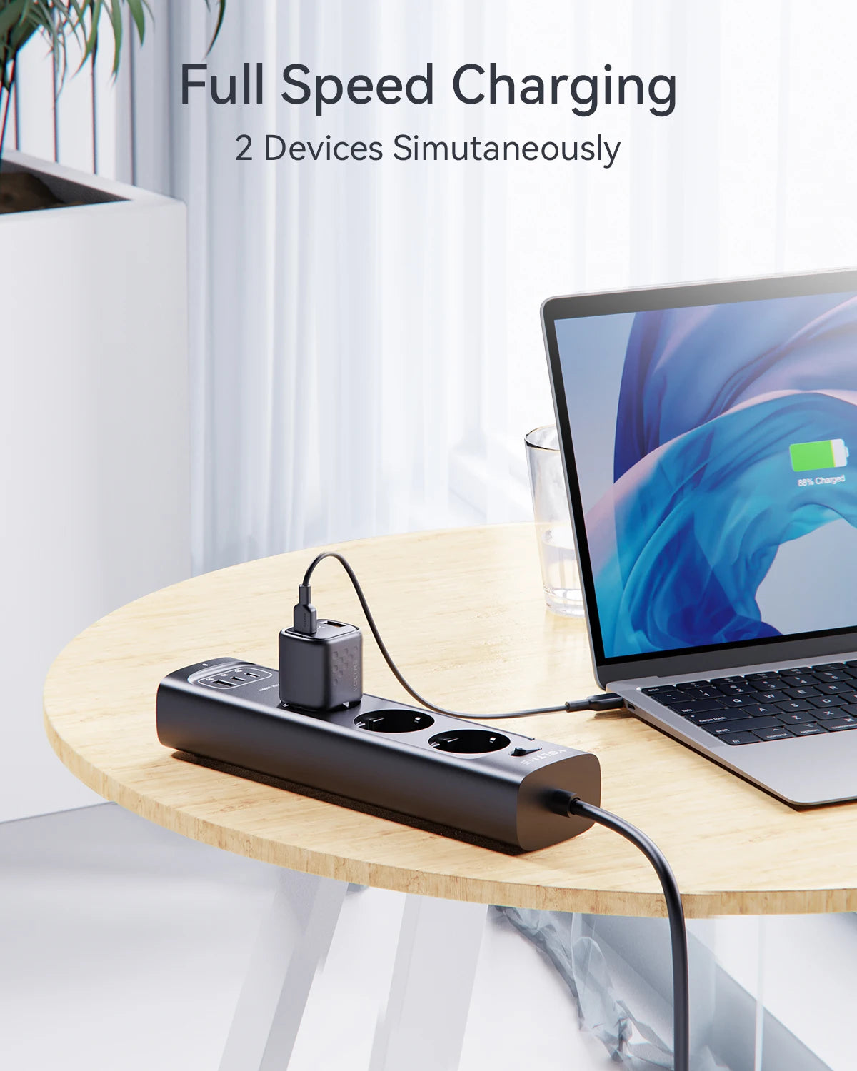 A charging station on a wooden table charges a laptop, displaying "89% Charged." Text above reads "Full Speed Charging, 2 Devices Simultaneously." Plant and curtain in the background.