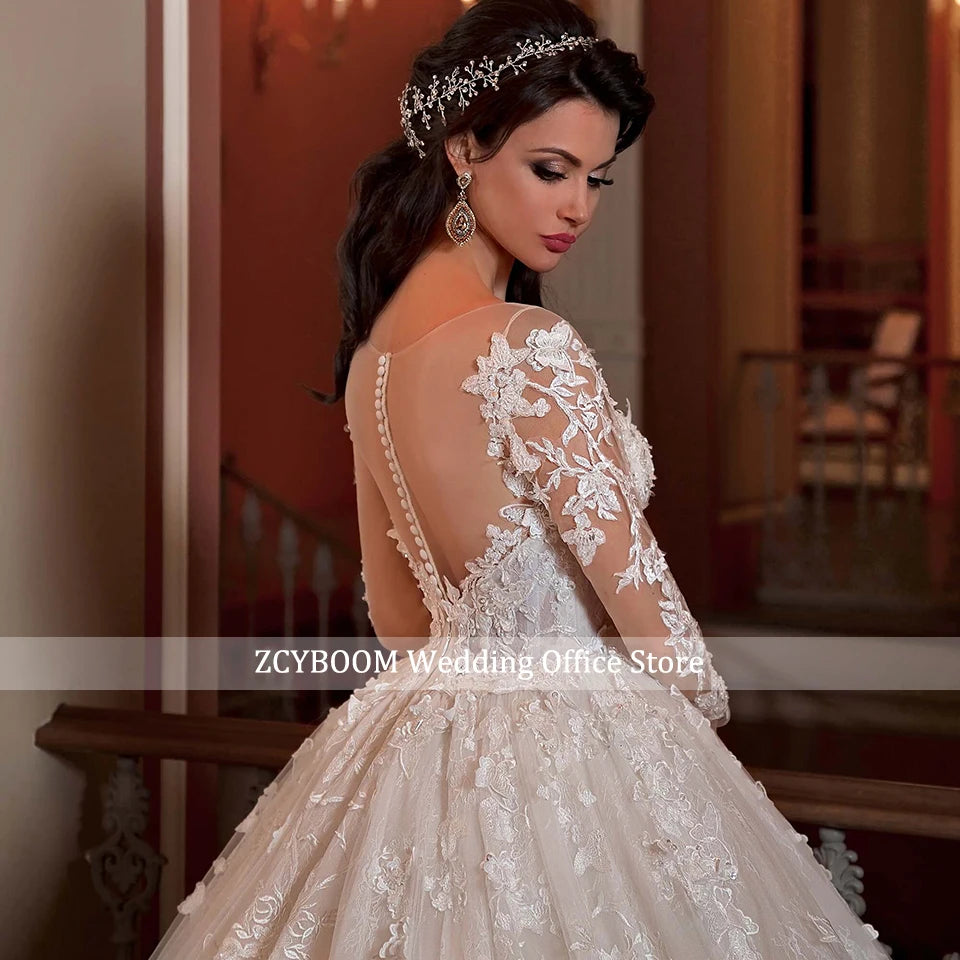 Elegant bride in a lace wedding dress with floral appliques and an open back, stands indoors. Her dark hair is styled with a decorative headband, and she wears chandelier earrings.