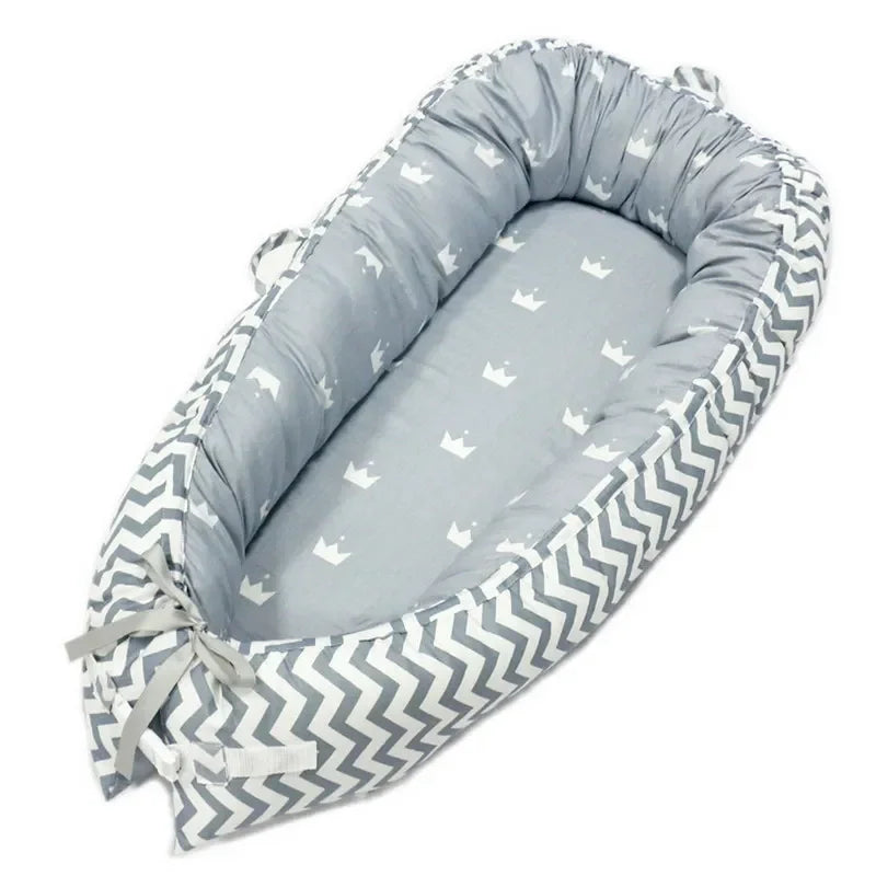 Gray baby nest with a crown pattern on the base and chevron sides, featuring a padded edge and tied ribbons at one end.