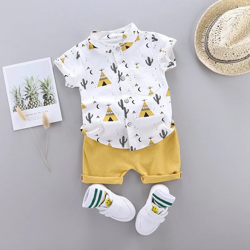 A cute toddler outfit with a white shirt featuring teepees and cacti, yellow shorts, white shoes with smiley faces, striped socks, a straw hat, and a pineapple print card.
