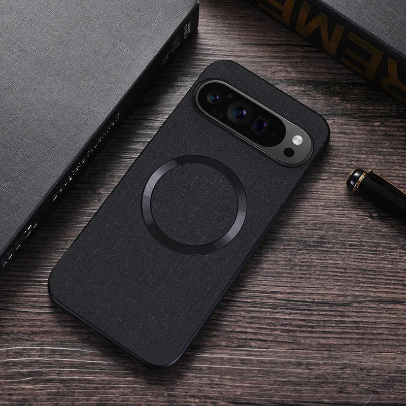 A black smartphone with a ring design on the back, placed on a wooden table. Nearby are a black book with gold lettering and a fountain pen.