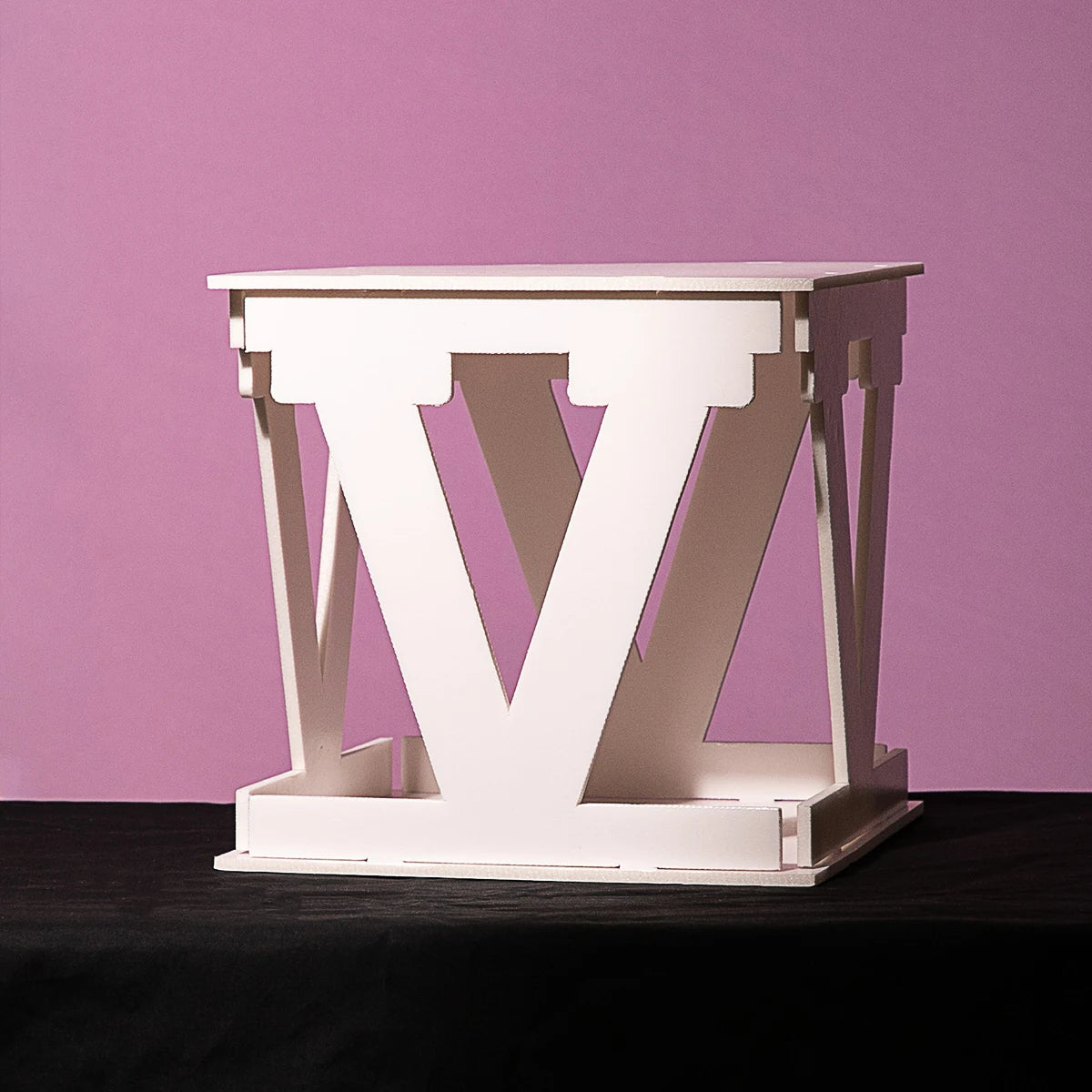 White geometric table with an inverted V-frame design on a black surface, set against a solid pink background.