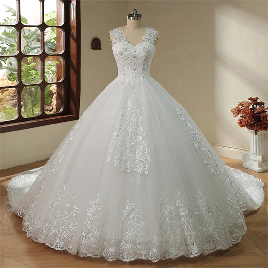 Elegant white ball gown wedding dress on mannequin, featuring delicate lace details and a voluminous skirt. Displayed near a window with a floral arrangement in the background.