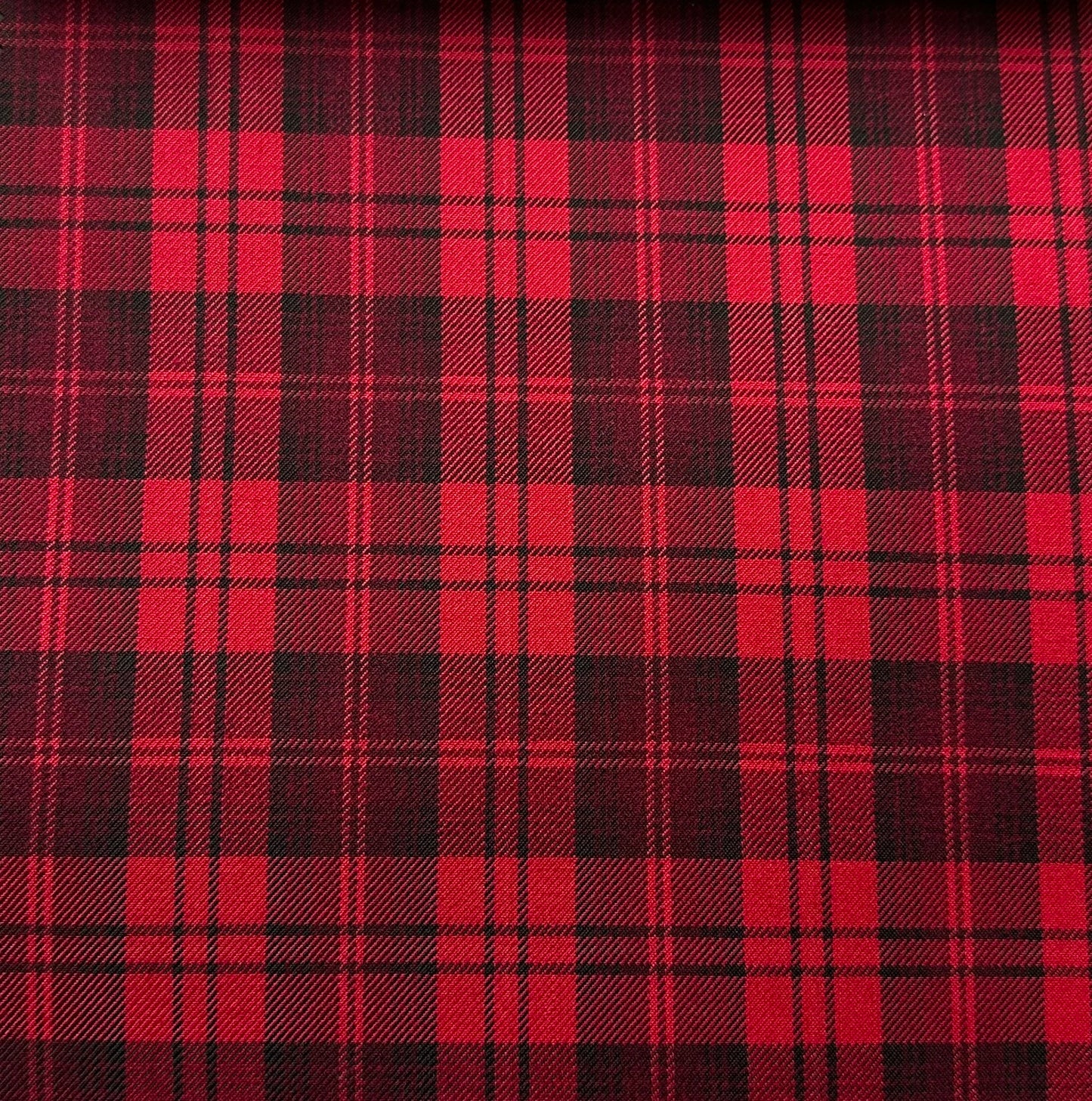 Red and black plaid fabric with a classic tartan pattern, featuring intersecting stripes creating a grid of squares. The design is symmetrical and evenly spaced.