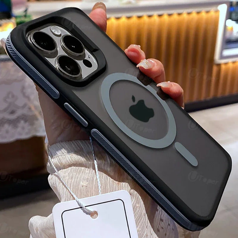 Hand holding a modern smartphone with a black case, featuring a camera cutout and circular design elements. Background shows a blurred interior setting with warm lighting.