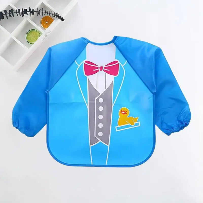 A blue bib designed like a tuxedo with a red bow tie, white shirt, and gray buttons. A yellow rubber duck graphic peeks from the pocket. A shelf with fruit slices decorates the wall above.