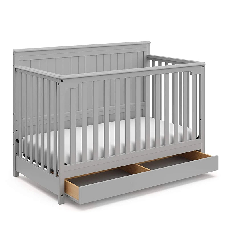 Gray wooden crib with slatted sides and a pull-out storage drawer underneath, featuring a simple, modern design.