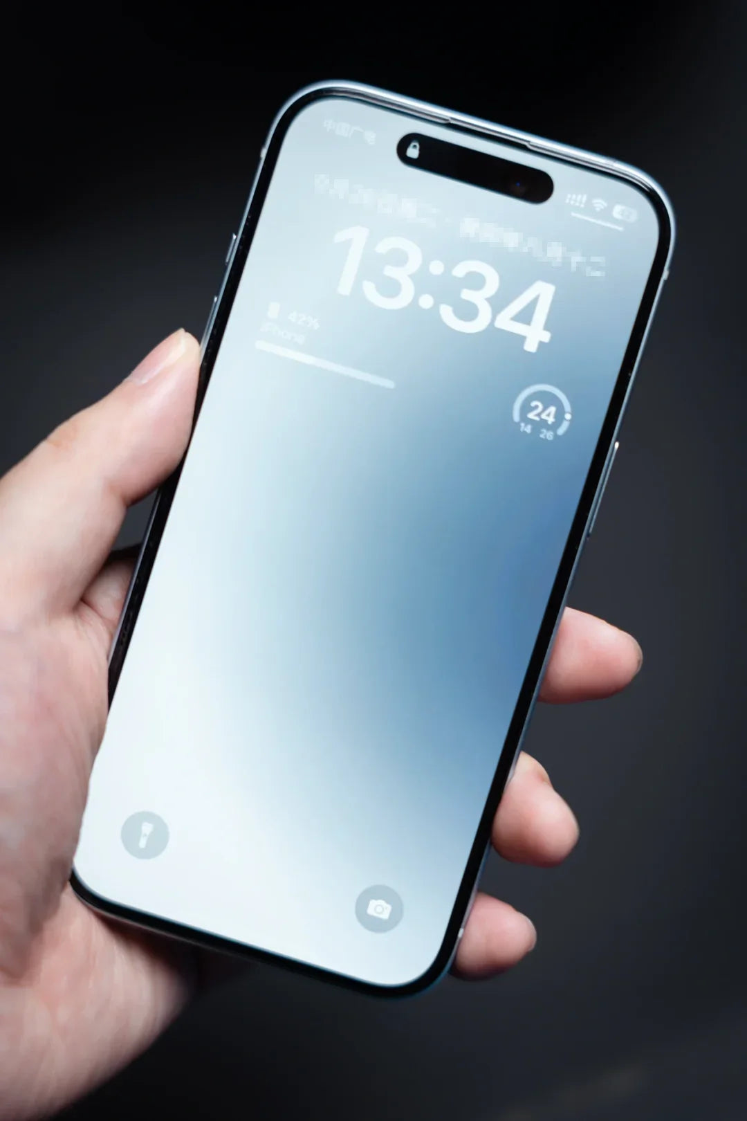 A person holds a smartphone displaying the lock screen, showing the time 13:34, with 42% battery remaining. The icons for flashlight and camera are visible at the bottom.