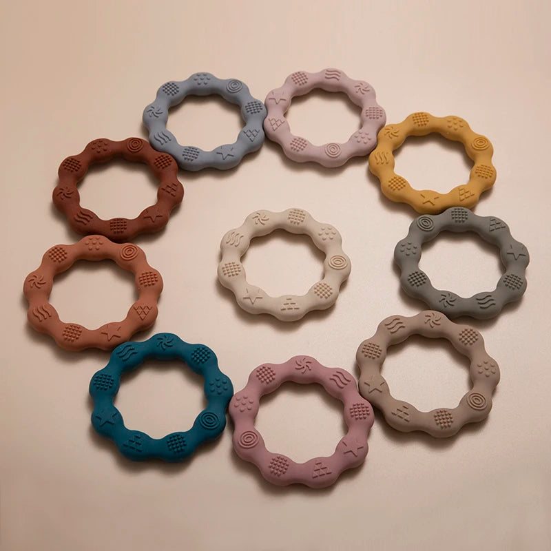 Colorful, textured teething rings form a circle on a neutral background. Rings are in shades of red, blue, white, grey, yellow, and purple, each with unique patterns.