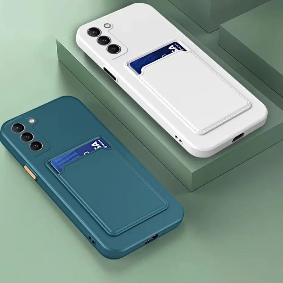 Two phone cases, one teal and one white, both with card holder slots containing a blue card, rest on a green geometric surface. Both cases have three camera cutouts.