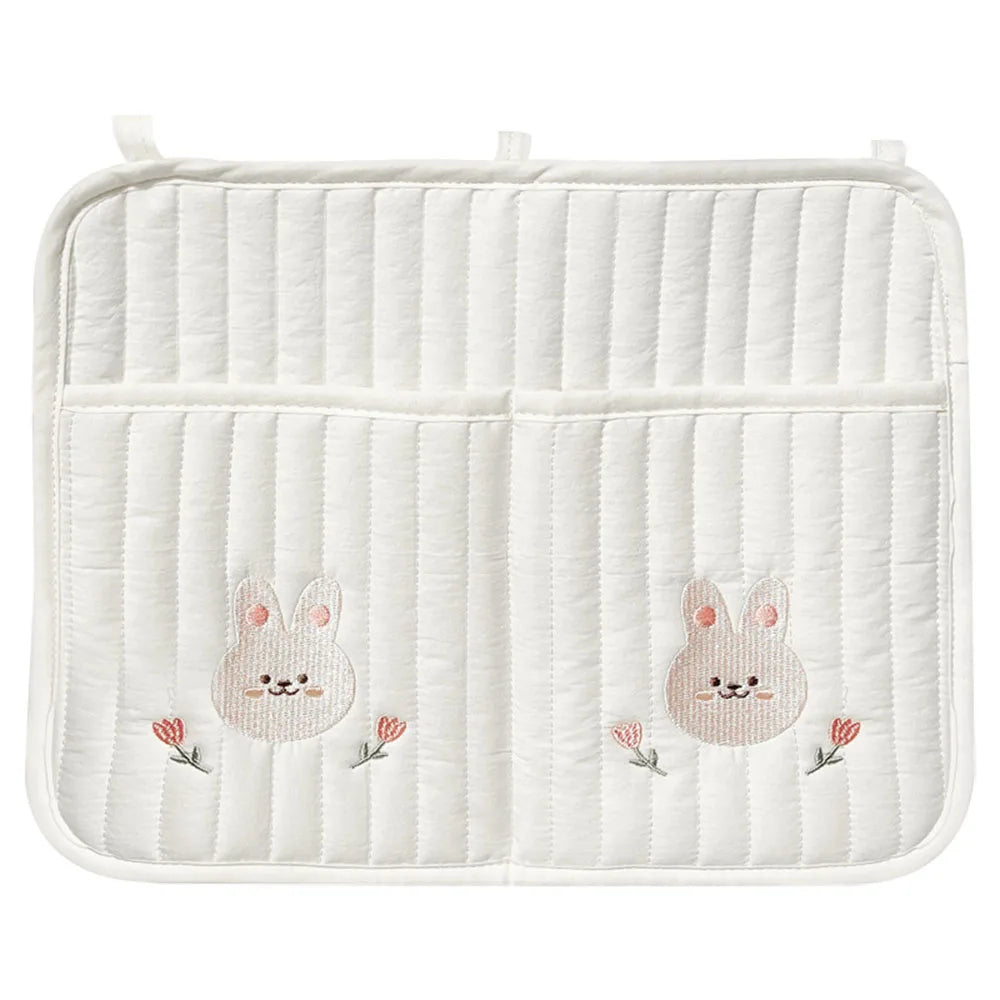 White quilted fabric with bunny faces and pink flower embroidery, featuring two pockets, and loops for hanging.