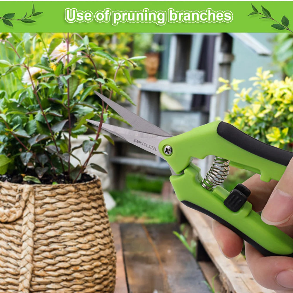 A hand uses green-handled pruning shears to trim a plant in a woven basket. The background shows a garden setting with various plants and greenery.