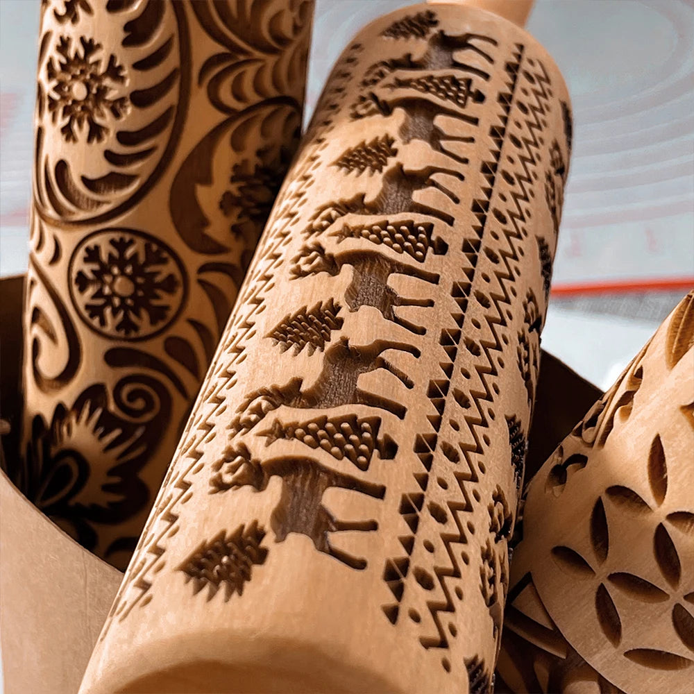 Close-up of intricately carved rolling pins with various patterns, including reindeer, trees, and snowflakes, used for embossing designs onto dough or pastries.