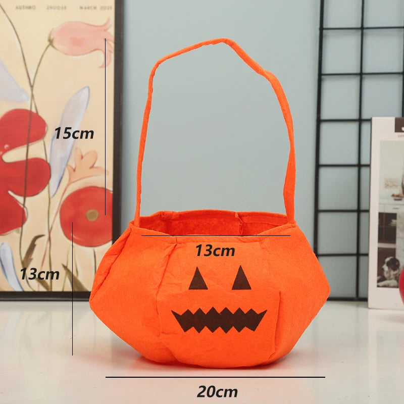 Orange felt pumpkin basket with black jack-o'-lantern face. Measures 20cm wide, 13cm tall, and 15cm with handle. Background includes floral artwork and blurred photo.