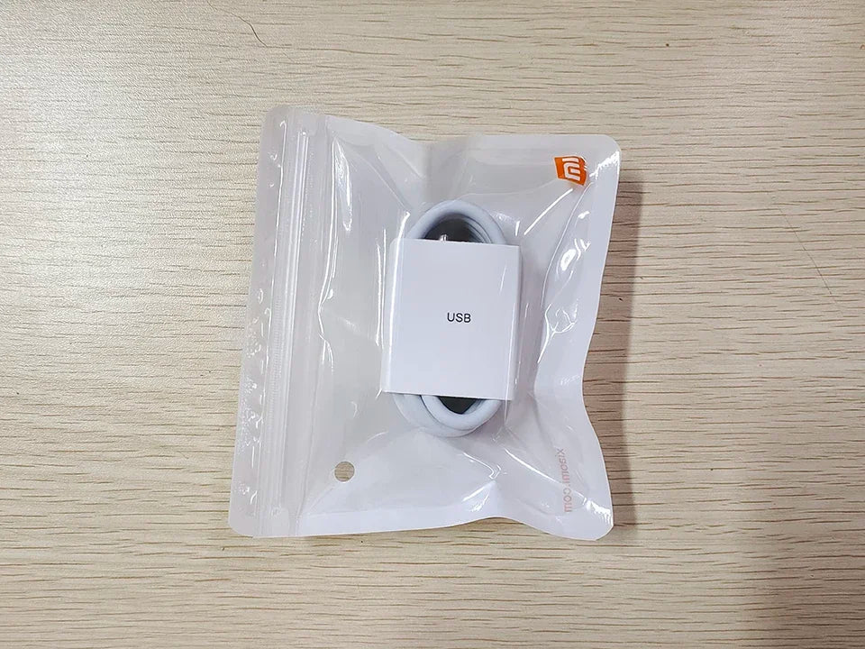A neatly coiled USB cable is in a sealed, clear plastic bag labeled "USB," sitting on a light wood surface.