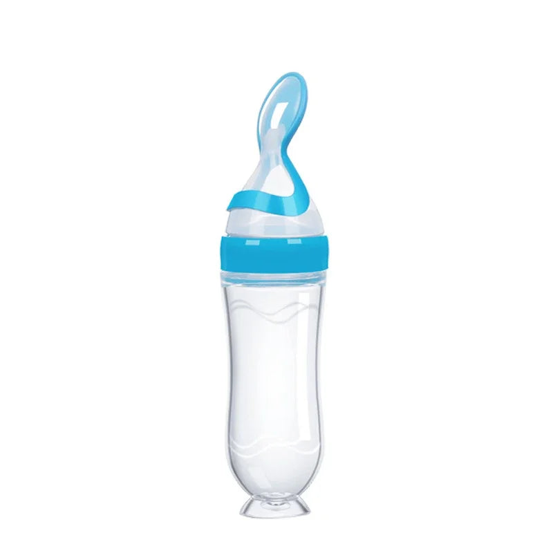 Clear baby feeding bottle with a blue lid and an attached spoon, designed for easy feeding. The bottle has a bulbous base and a slim neck.