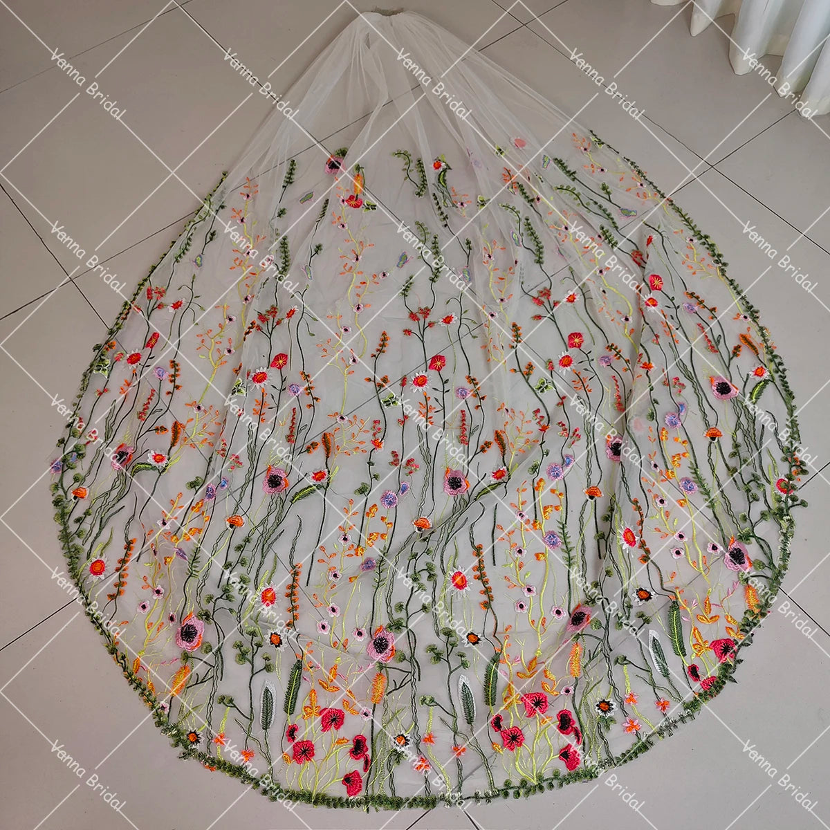 A round, sheer white bridal veil with intricate floral embroidery in vibrant colors including red, pink, orange, and green, displayed on a tiled floor.